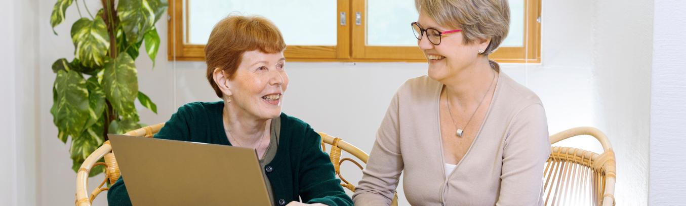 Kaksi naista pöydän ääressä, toisen edessä kannettava tietokone.